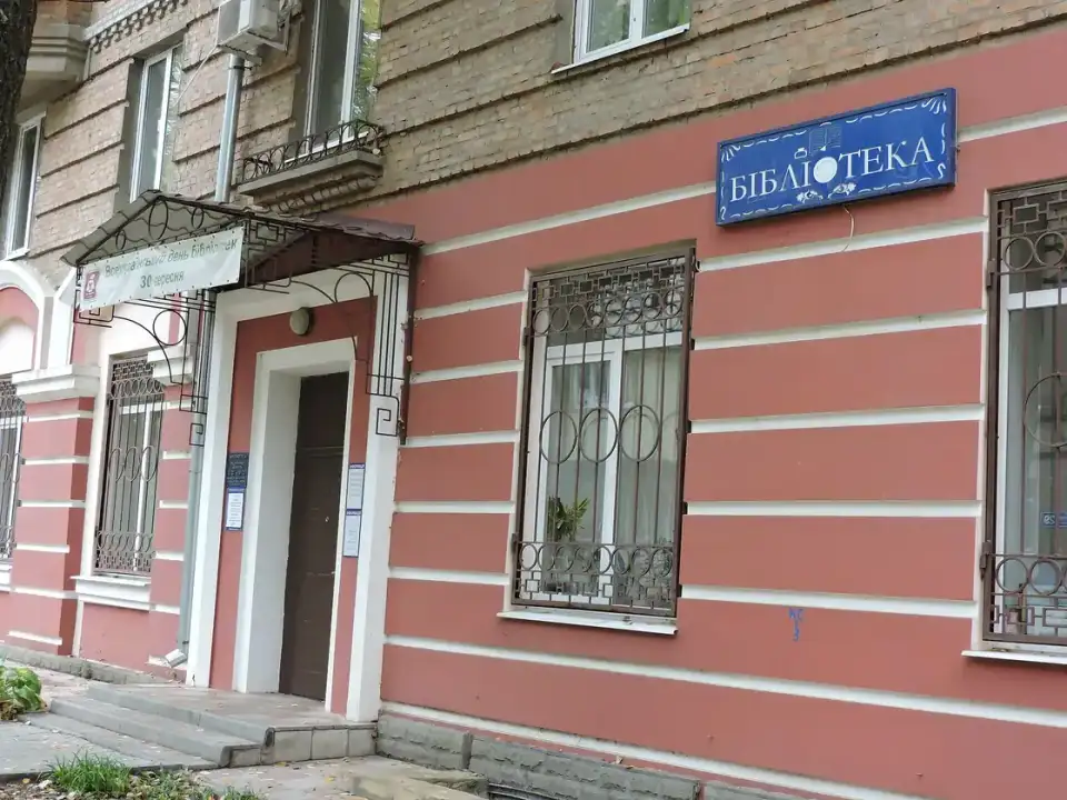 Порожній вхід до бібліотеки в рожево-цегляному фасаді на Данилевського, поруч із синьою вивіскою «Бібліотека» та вікнами з ґратами