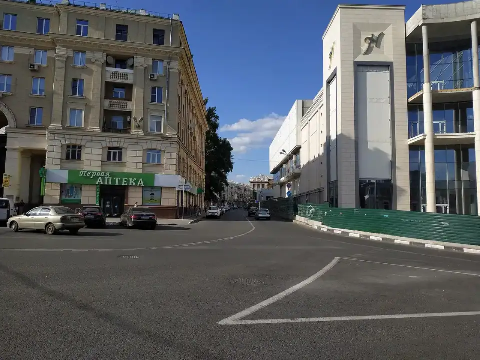 Літній міський фрагмент вулиці Григорія Сковороди зі світлими фасадами, синім небом, кількома автомобілями та поодинокими людьми вдалині