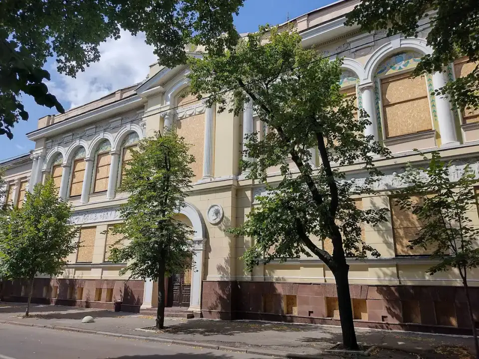 Жовтий фасад Харківського художнього музею з білим декором, закритими вікнами й зеленими деревами вздовж вулиці