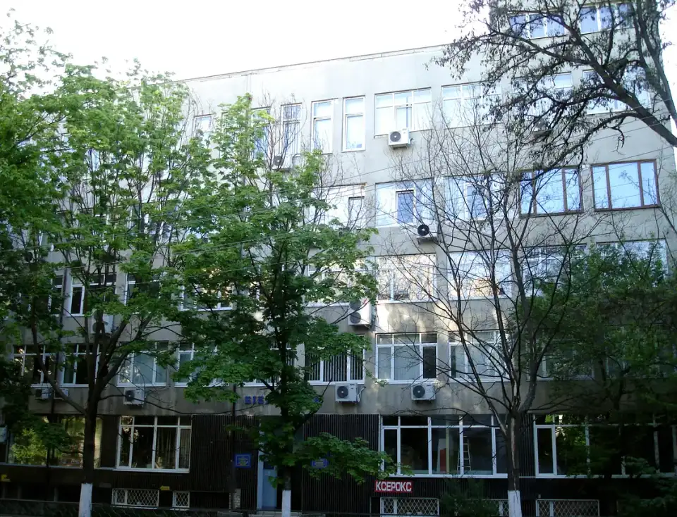 Сірий фасад Харківської обласної бібліотеки для дітей та юнацтва за зеленими деревами; людей у кадрі немає, біля входу частково видно синю назву установи