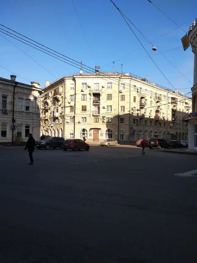Світлий багатоповерховий кутовий фасад на Кооперативній вулиці з червоною бібліотечною вивіскою над входом, кількома автомобілями й поодинокими перехожими