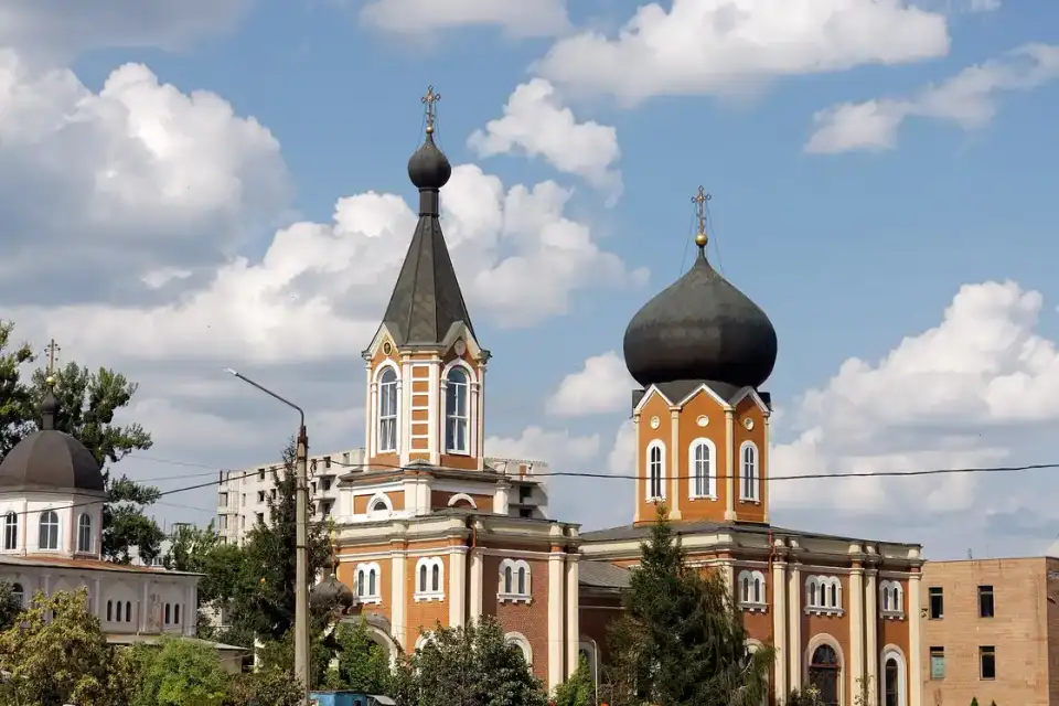 Цегляний Петро-Павлівський храм із високою дзвіницею, темною банею та білими деталями під великими літніми хмарами; людей у кадрі немає