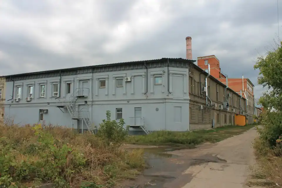 Сірий двоповерховий фасад колишнього парового млина на Юрʼївській із цегляним виробничим корпусом позаду, похмурим небом і без людей у кадрі